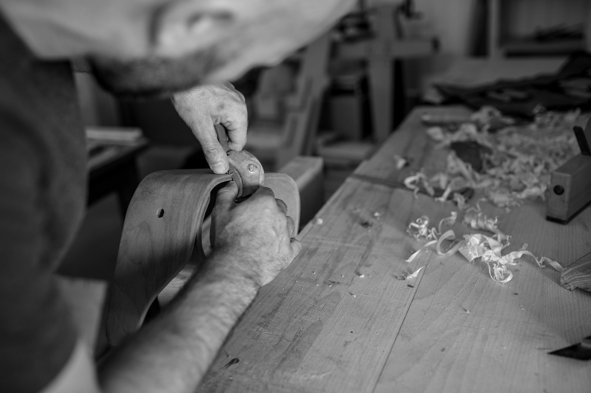 Ébéniste façonnant à la main une pièce de bois courbe dans l’atelier
